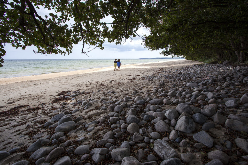 Bild på två kvinnor som promenerar längs stranden på Österlen